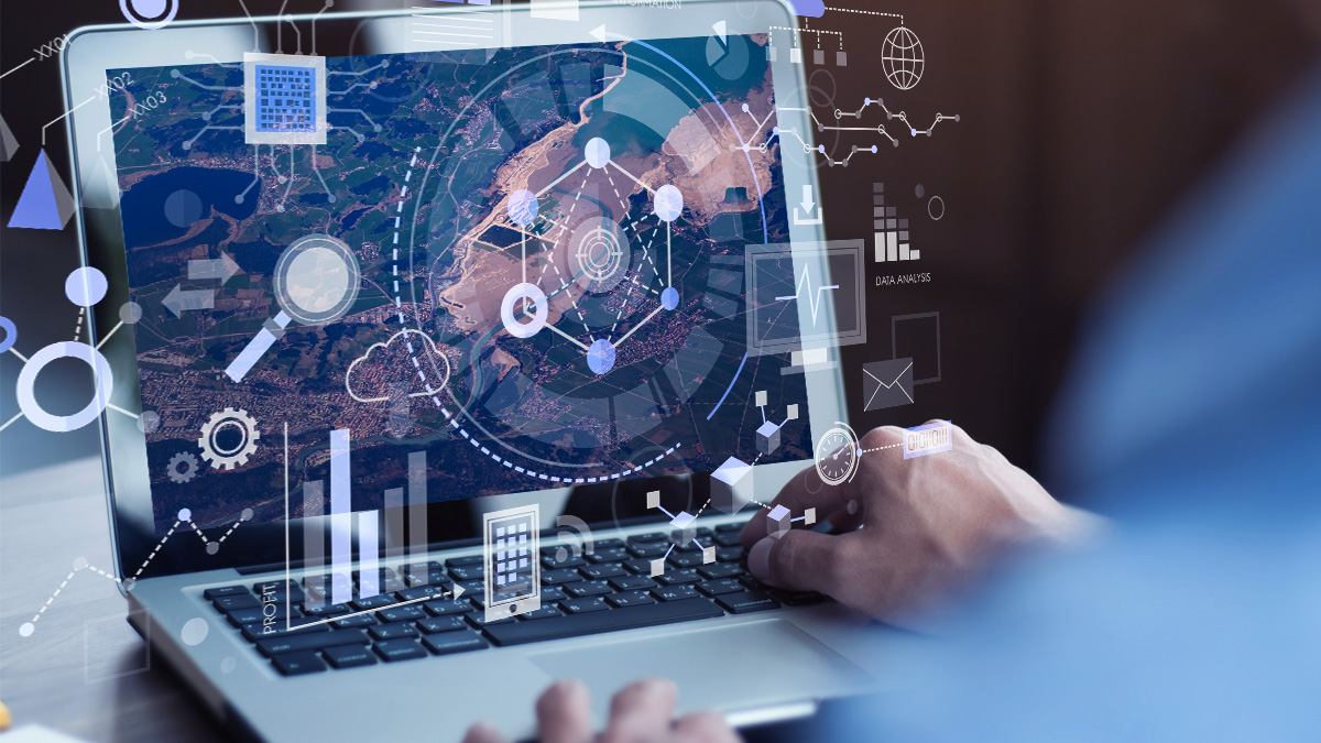A GIS professional analyzes satellite imagery and geospatial data on a laptop, enhanced with digital overlays for data visualization, location intelligence, and risk modeling.
